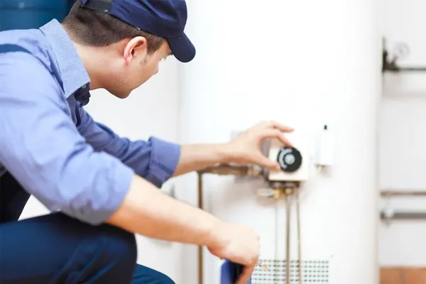 a plumber in a blue shirt kneeling, servicing a water heater unit, emphasizing plumbing repairs and installations in Fresno County